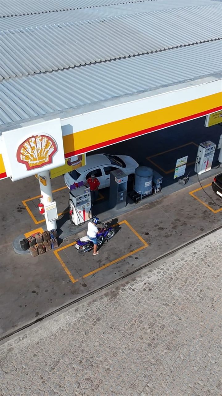 Vista de cima das bombas do Posto Bela Vista, com frentista abastecendo carro e moto